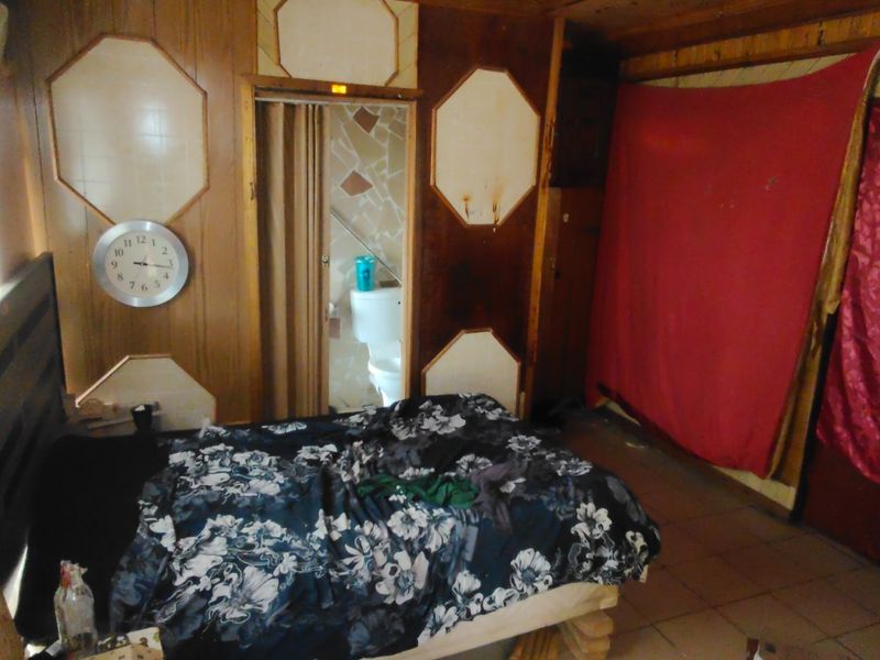 A bedroom featuring wood-paneled walls and tiled flooring, requiring significant cosmetic updates and repairs to improve the overall condition and aesthetic appeal.