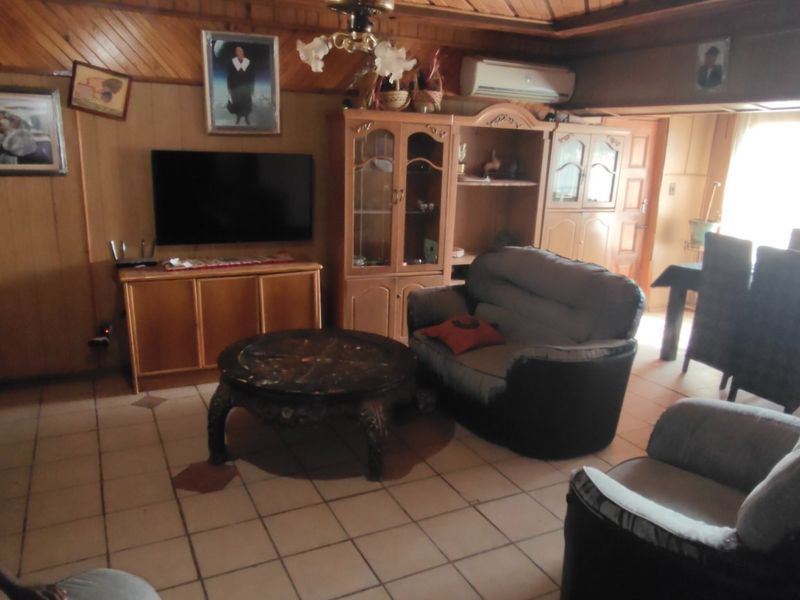 Open-plan living and dining area featuring wood-paneled walls, timber ceilings, and tiled flooring, equipped with a wall-mounted air conditioning unit.
