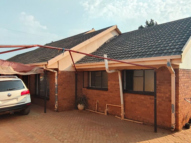 Front exterior view of a face brick house featuring a tiled roof, paved driveway, and an attached metal carport structure.