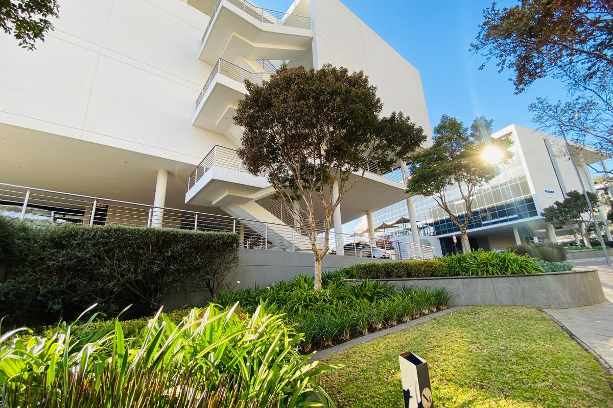 A modern commercial building exterior featuring a prominent external staircase, clean white facade, and well-maintained landscaped garden areas.