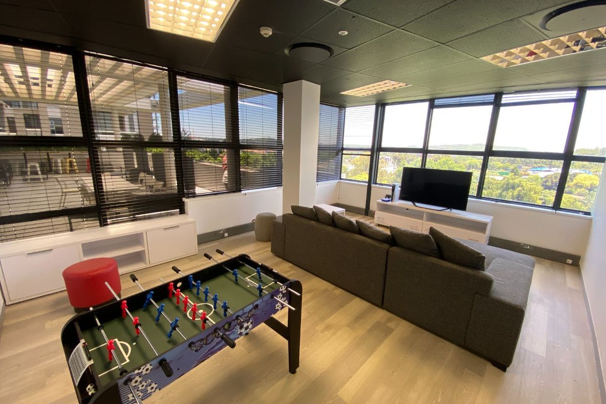 A modern, well-lit commercial lounge area featuring large windows with venetian blinds, laminate flooring, and a suspended ceiling with recessed lighting.