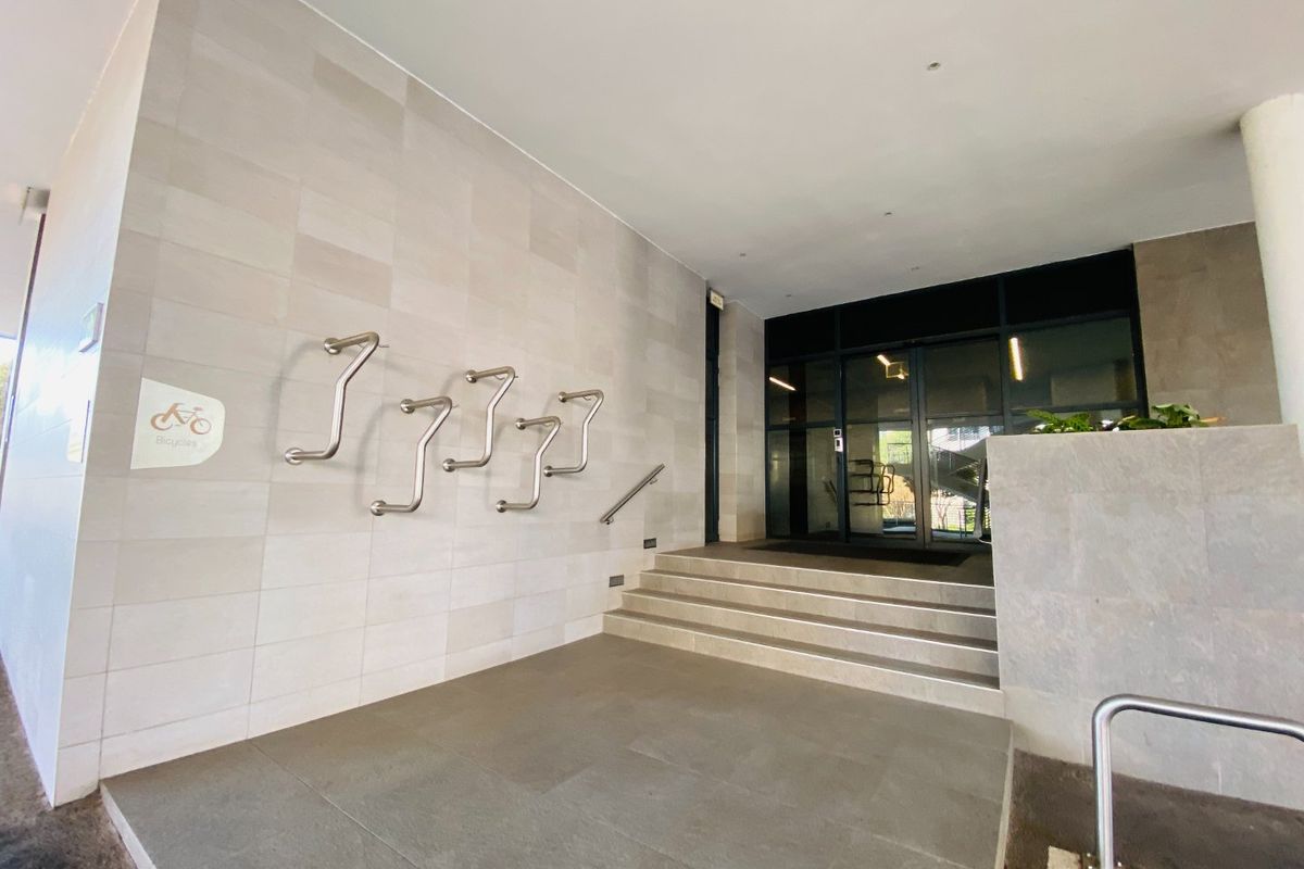 Modern commercial building entrance featuring stone wall cladding, stainless steel bicycle racks, and glass doors with concrete steps.