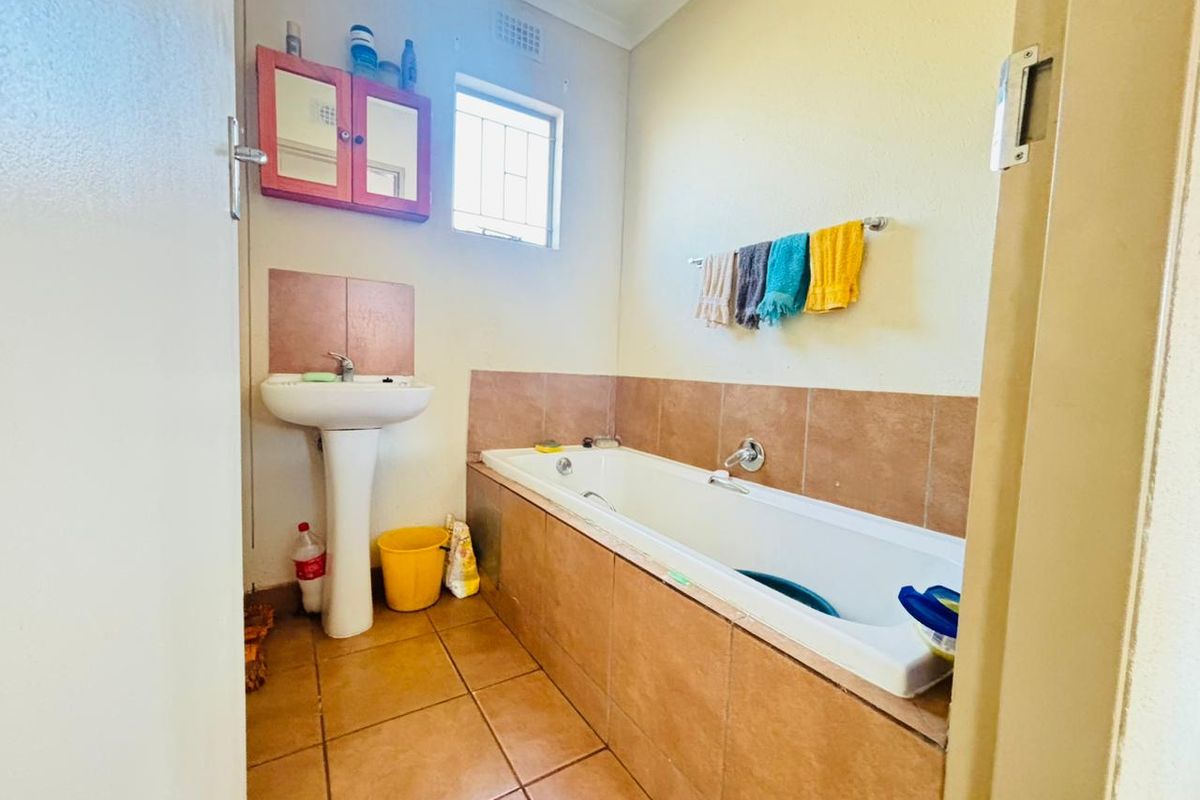 A functional bathroom featuring a built-in bathtub, pedestal basin, and tiled finishes, offering a practical layout with potential for modern updates.