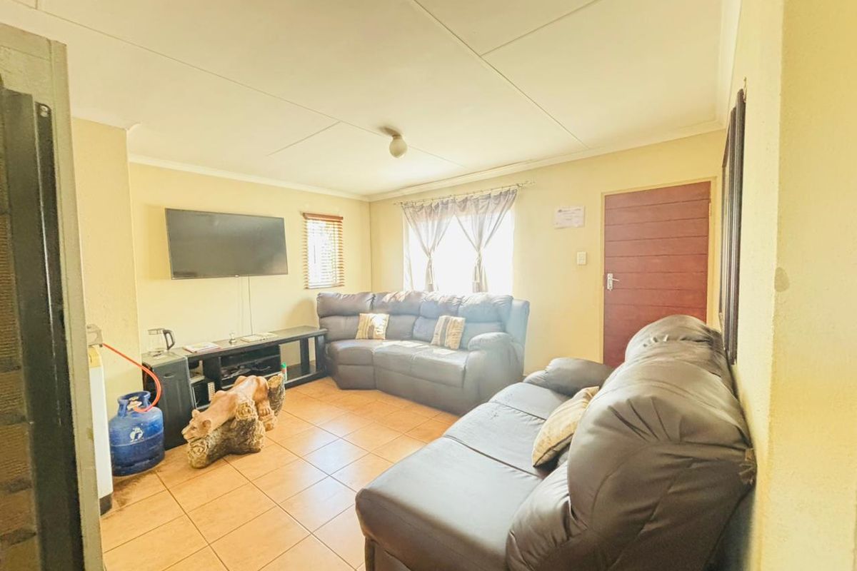 A functional living room featuring tiled flooring, a timber door, and window blinds, providing a comfortable and practical space for relaxation.