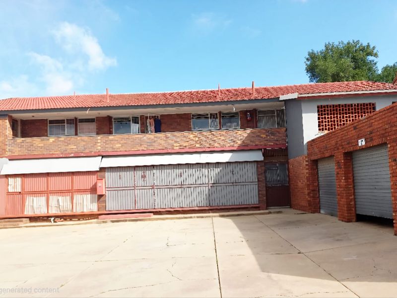 Exterior view of an apartment complex featuring brick facade, tiled roof, and integrated garage units with a paved driveway area.