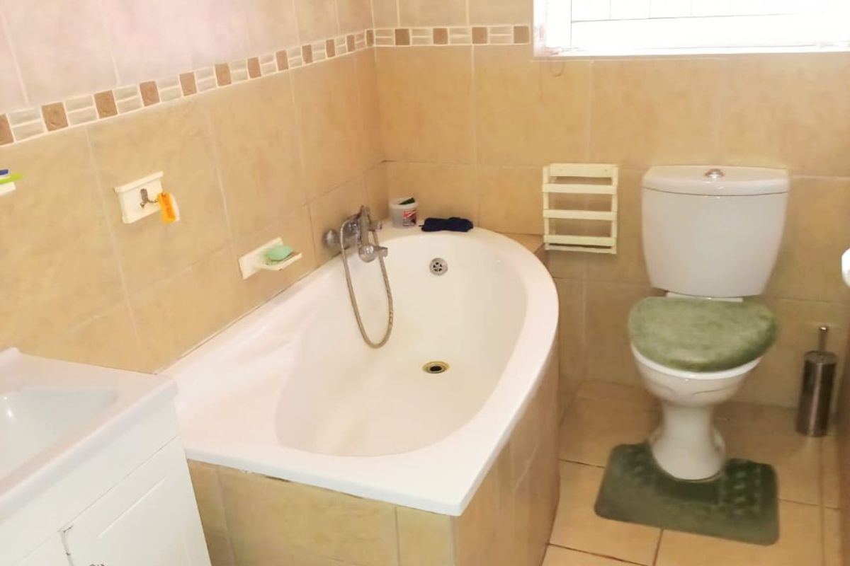 A functional bathroom featuring a built-in bathtub with shower mixer, a standard toilet, and a vanity cabinet with integrated basin.