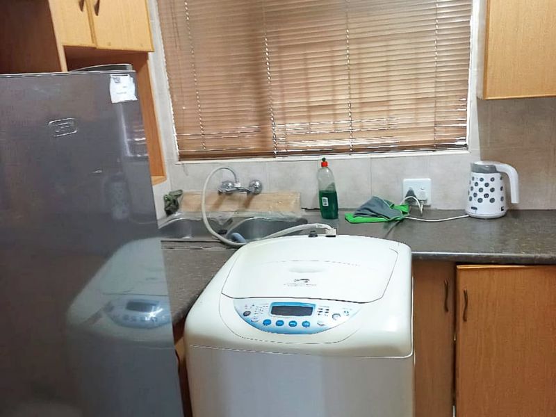 A functional laundry area featuring built-in wooden cabinetry, a stainless steel double sink, and tiled flooring with a window providing natural light.