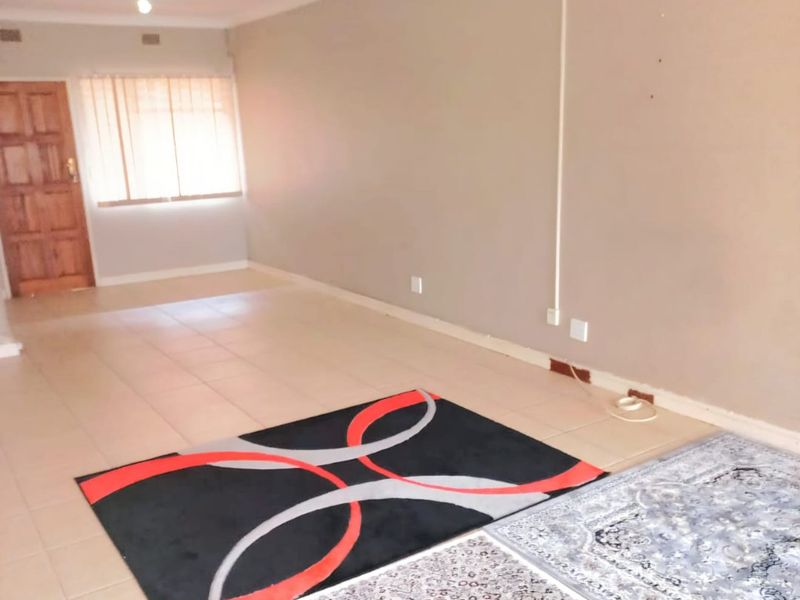 A spacious, open-plan living area featuring neutral wall tones, tiled flooring, and a wooden entrance door, providing a versatile space for customization.