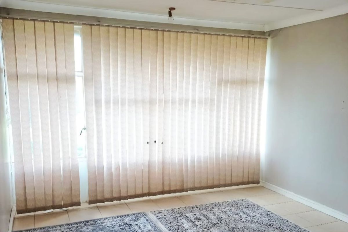 A vacant bedroom featuring tiled flooring, vertical window blinds, and visible water damage on the ceiling.