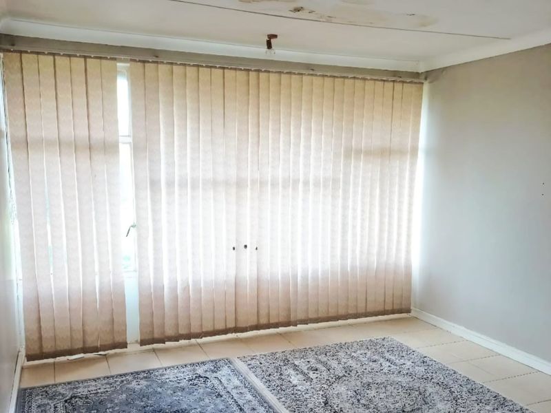 A vacant bedroom featuring tiled flooring, vertical window blinds, and visible water damage on the ceiling.