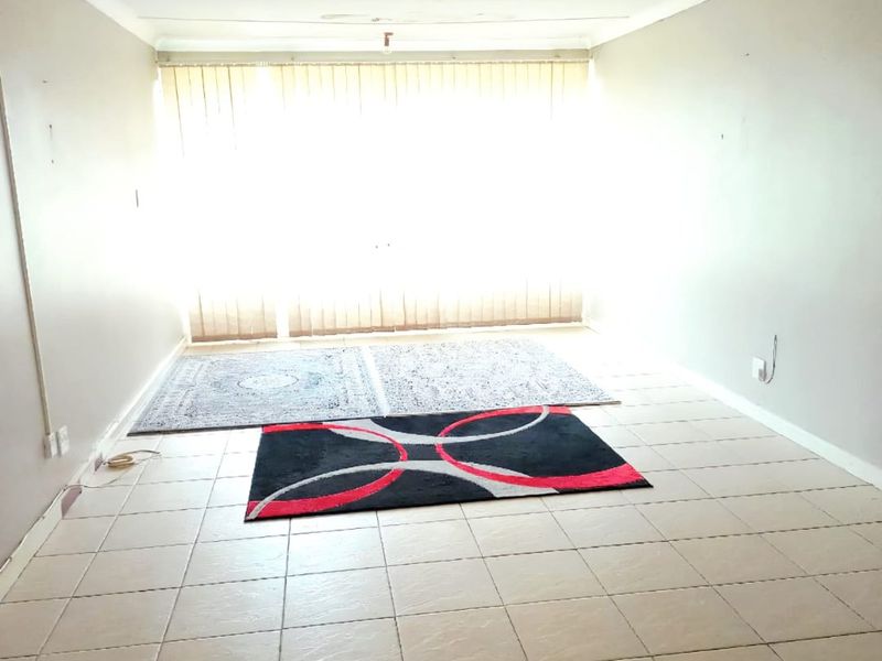 An open-plan living area featuring tiled flooring, vertical blinds, and basic lighting fixtures, offering a blank canvas for potential renovation.