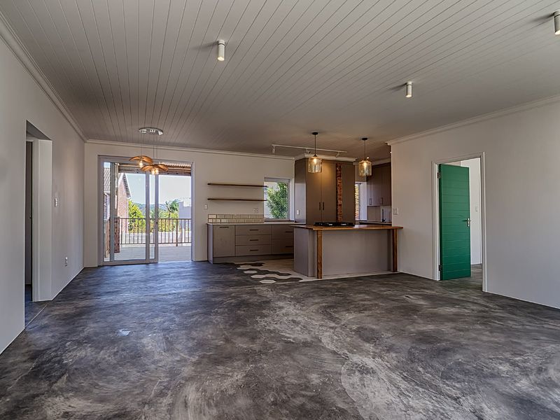 Spacious open-plan living and kitchen area featuring polished concrete floors, tongue and groove ceilings, and direct access to an outdoor patio.