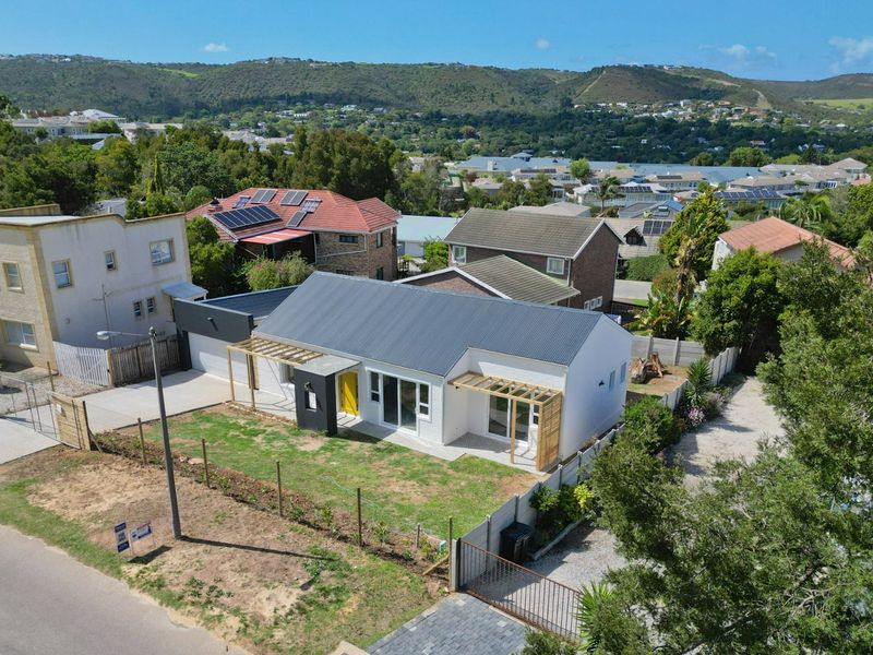 Aerial view of a modern single-story house featuring a metal roof, timber pergolas, and a double garage, set within a residential neighborhood.