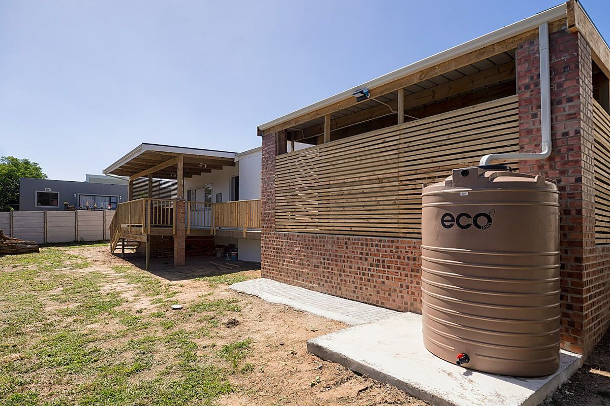 Rear exterior view featuring a brick structure with timber screening, a large water storage tank on a concrete base, and an elevated timber deck.