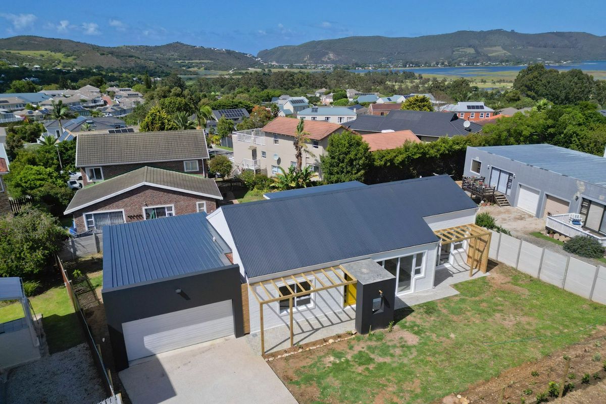 Aerial view of a modern residential property featuring a dark metal roof, attached garage, timber pergolas, and a spacious garden area.