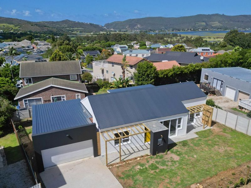 Aerial view of a modern residential property featuring a dark metal roof, attached garage, timber pergolas, and a spacious garden area.
