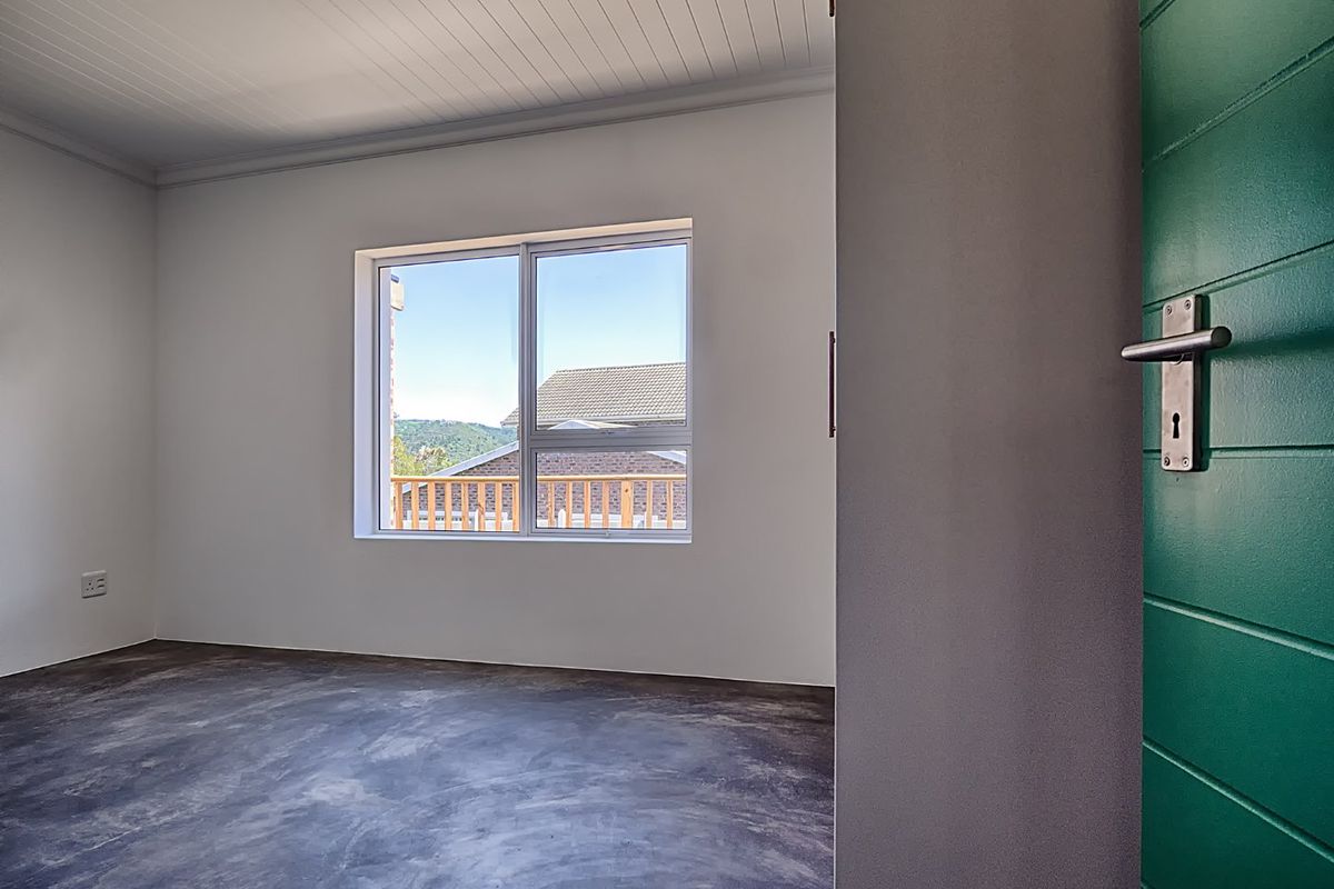 A bright, empty bedroom featuring polished concrete flooring, a tongue and groove ceiling, and a green door, offering a clean, modern aesthetic.