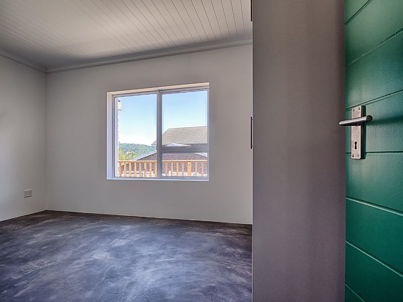 A bright, empty bedroom featuring polished concrete flooring, a tongue and groove ceiling, and a green door, offering a clean, modern aesthetic.