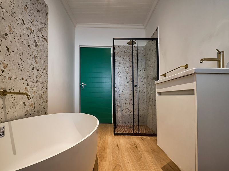 Modern bathroom featuring a freestanding bathtub, walk-in shower with glass enclosure, vanity unit with brass fixtures, and stylish terrazzo-style wall tiling.