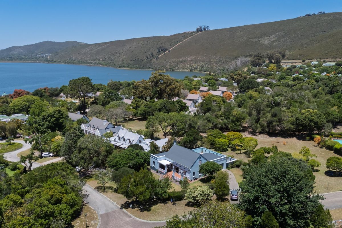 Aerial view of a residential property featuring a metal roof, covered veranda, and paved driveway, set within a lush, green coastal landscape.