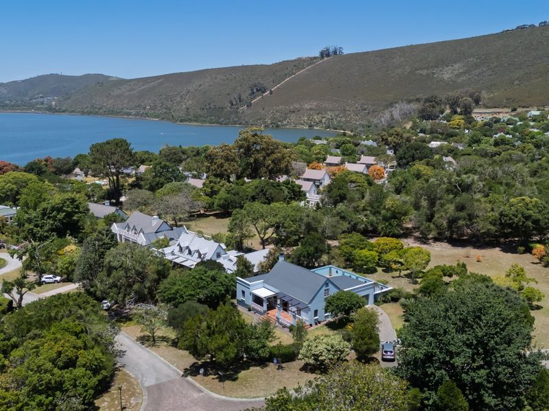 Aerial view of a residential property featuring a metal roof, covered veranda, and paved driveway, set within a lush, green coastal landscape.