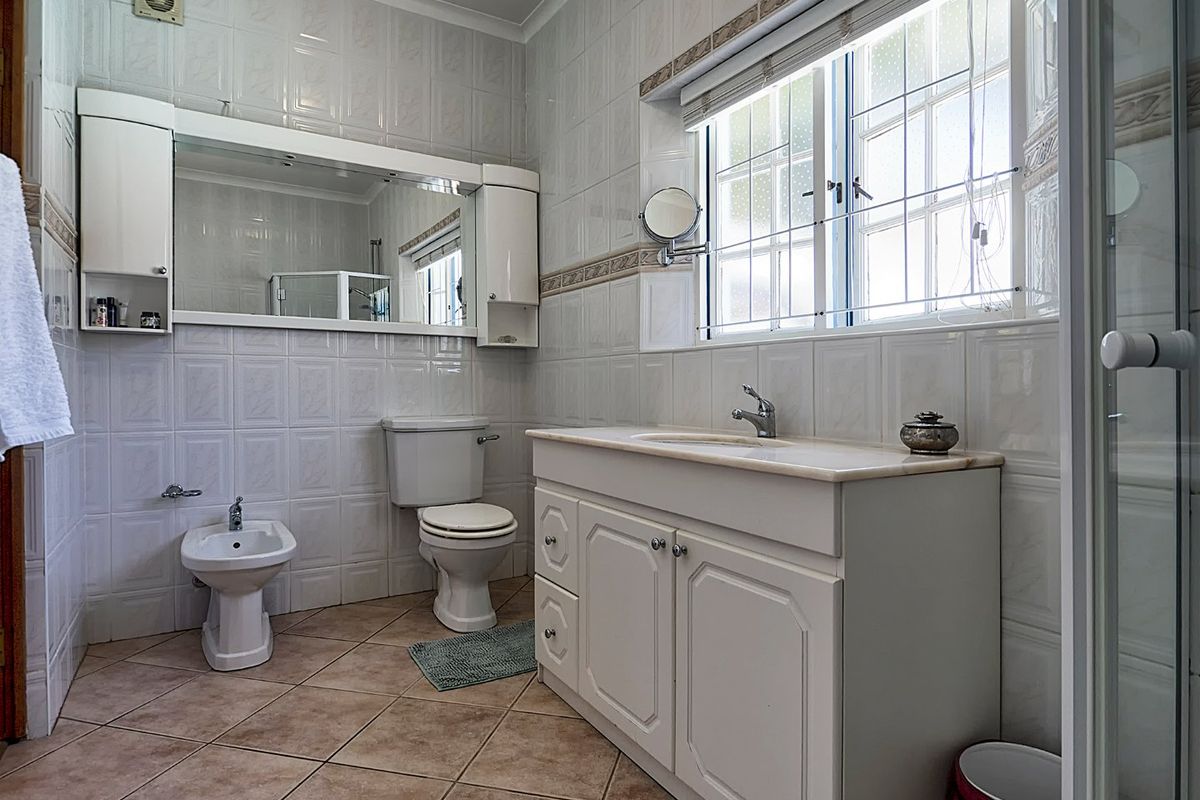 A functional bathroom featuring a vanity cabinet, integrated sink, toilet, bidet, and wall-mounted mirror cabinet with tiled finishes throughout.