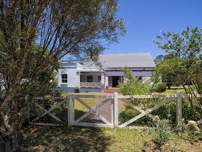 Charming single-story house featuring a corrugated metal roof, a welcoming covered veranda with timber balustrades, and a classic white picket fence.