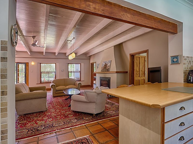 Spacious open-plan living area featuring exposed timber ceiling beams, a cozy fireplace, and terracotta flooring, seamlessly connecting to the kitchen space.