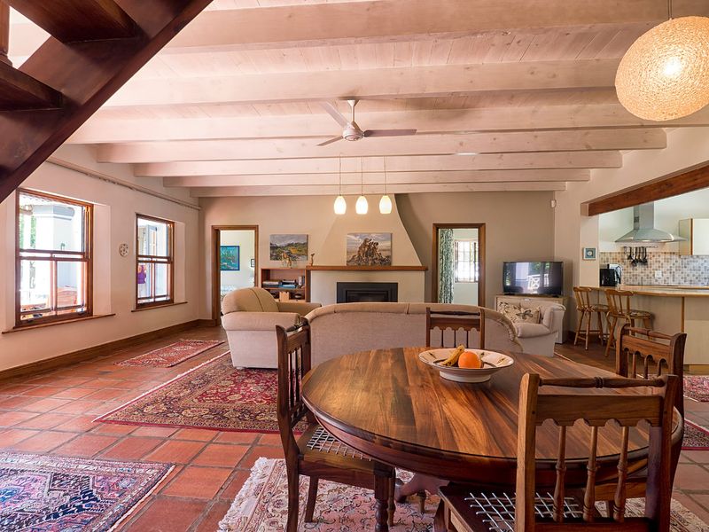 Spacious open-plan living and dining area featuring exposed timber ceiling beams, terracotta flooring, and a central built-in fireplace, seamlessly connecting to the kitchen.