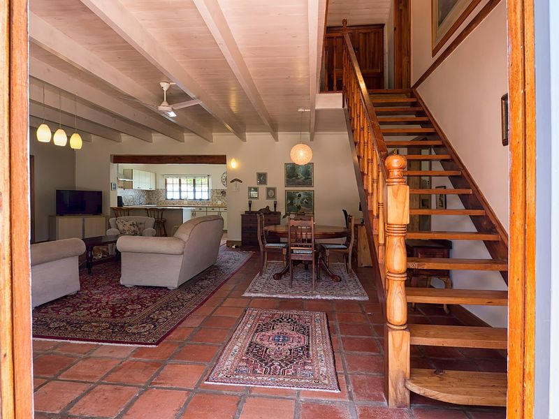 Spacious open-plan living and dining area featuring exposed timber ceiling beams, terracotta flooring, and a prominent timber staircase leading to the upper level.