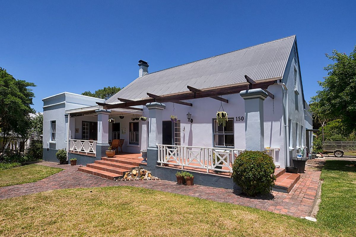 A charming single-story residence featuring a corrugated metal roof, a covered brick patio with timber pergola, and a well-maintained front garden.
