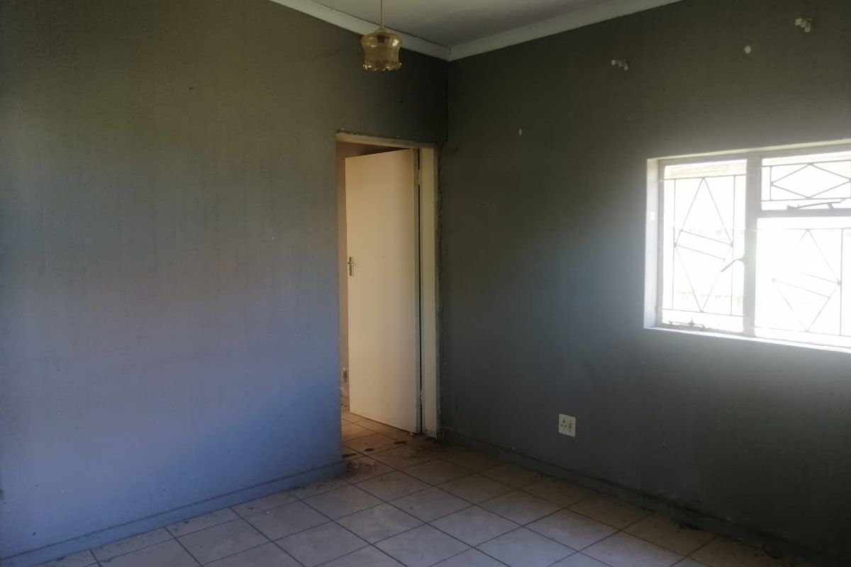An empty bedroom featuring tiled flooring, burglar bars on the window, and dark grey painted walls in need of refurbishment.