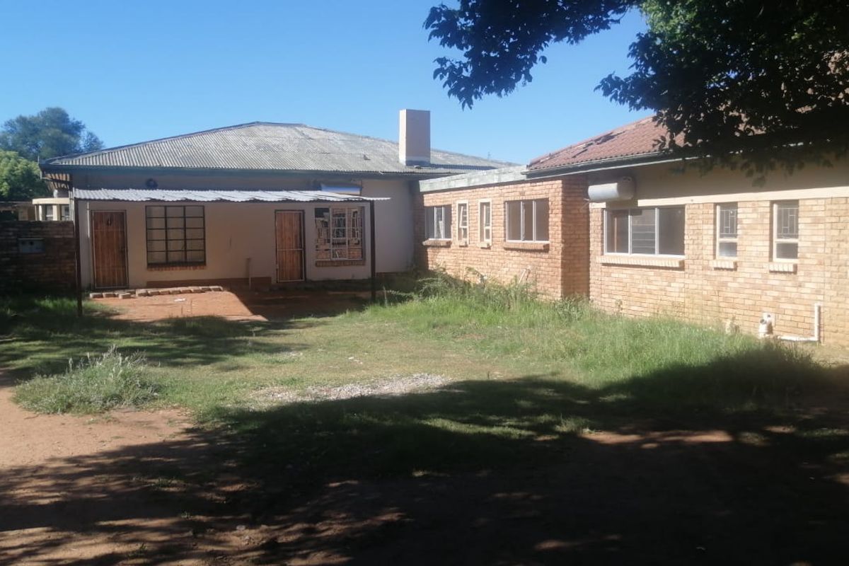 Rear view of the property showing a brick facade, covered patio area, and a large backyard with overgrown grass.