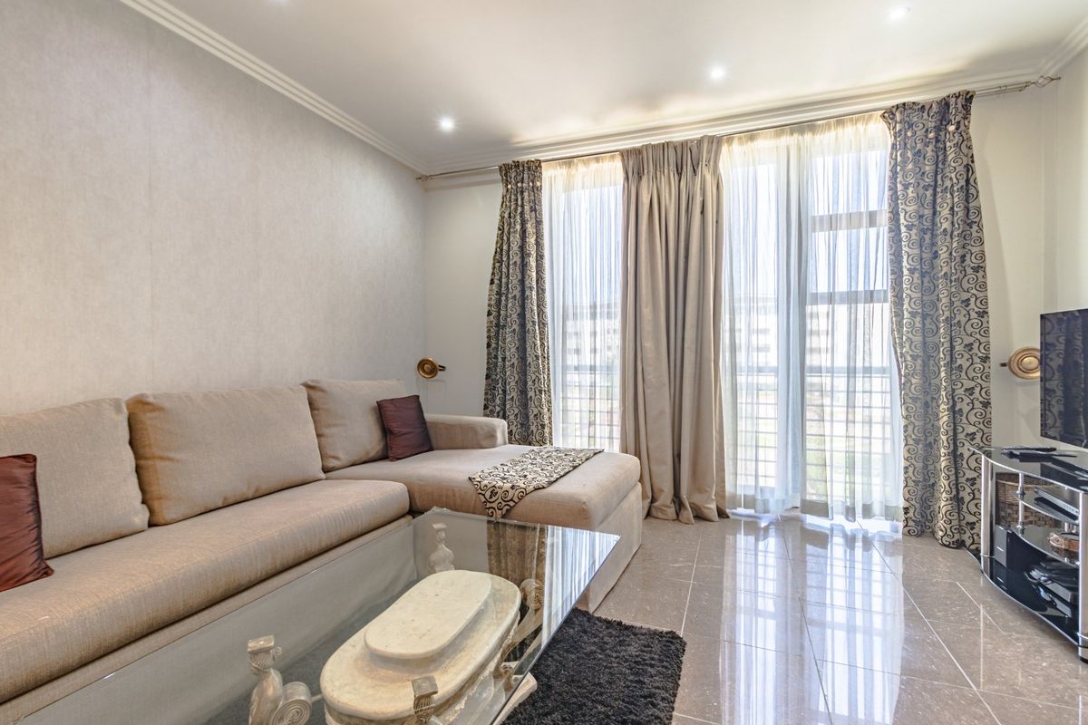 A well-maintained living room featuring polished tile flooring, recessed downlighting, crown molding, and large sliding glass doors leading to a balcony.