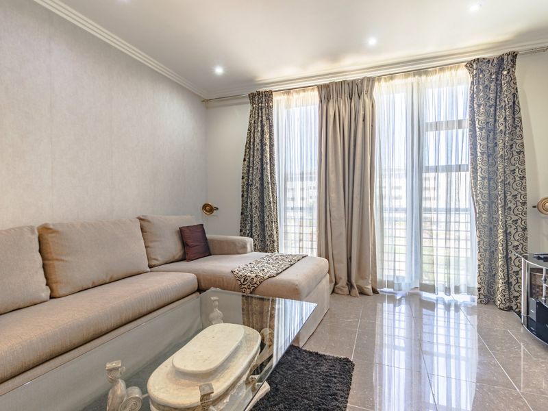 A well-maintained living room featuring polished tile flooring, recessed downlighting, crown molding, and large sliding glass doors leading to a balcony.