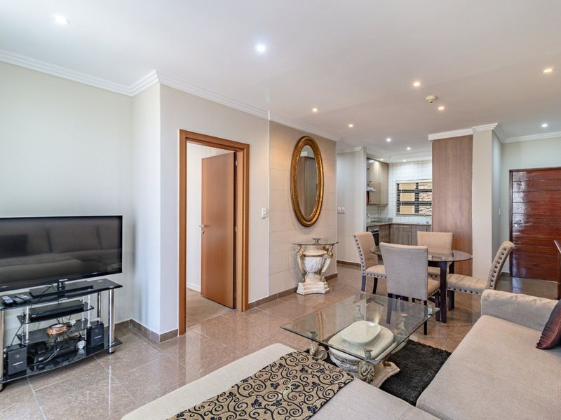 An open-plan living and dining area featuring tiled floors, recessed lighting, and a seamless transition into a modern kitchen with built-in cabinetry.