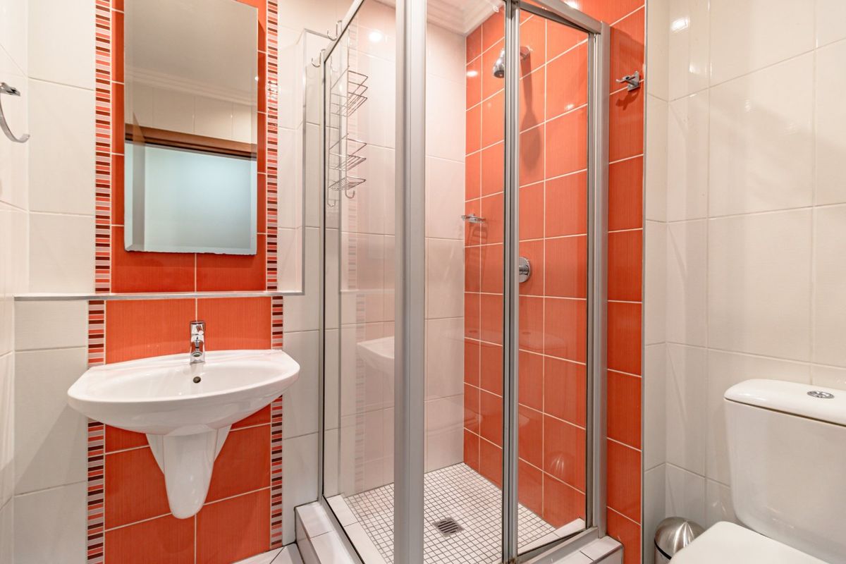 Compact bathroom featuring a shower enclosure, wall-mounted basin, and toilet with vibrant orange and white tiled finishes.