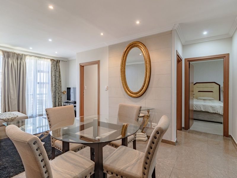 An open-plan living and dining area featuring tiled flooring, recessed downlighting, and access to an adjoining bedroom and balcony.