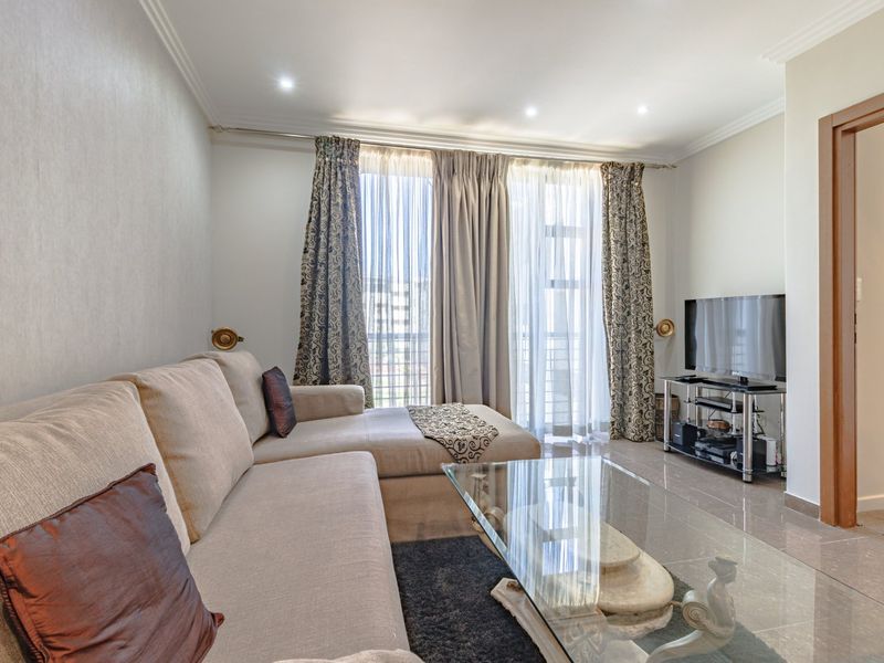 A well-lit living room featuring tiled flooring, recessed downlighting, and a large sliding glass door providing access to the balcony.