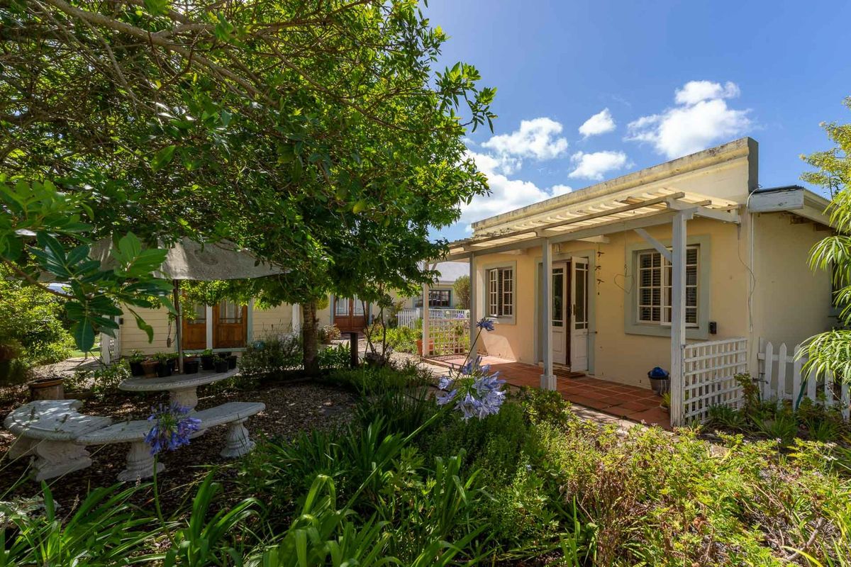 A charming rear exterior view featuring a covered patio with terracotta tiles, timber-framed windows, and a lush, established garden setting.
