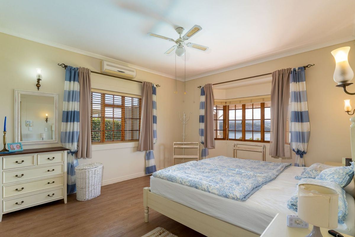 A well-maintained bedroom featuring timber-look flooring, a ceiling fan, split-system air conditioning, and a bay window with views.