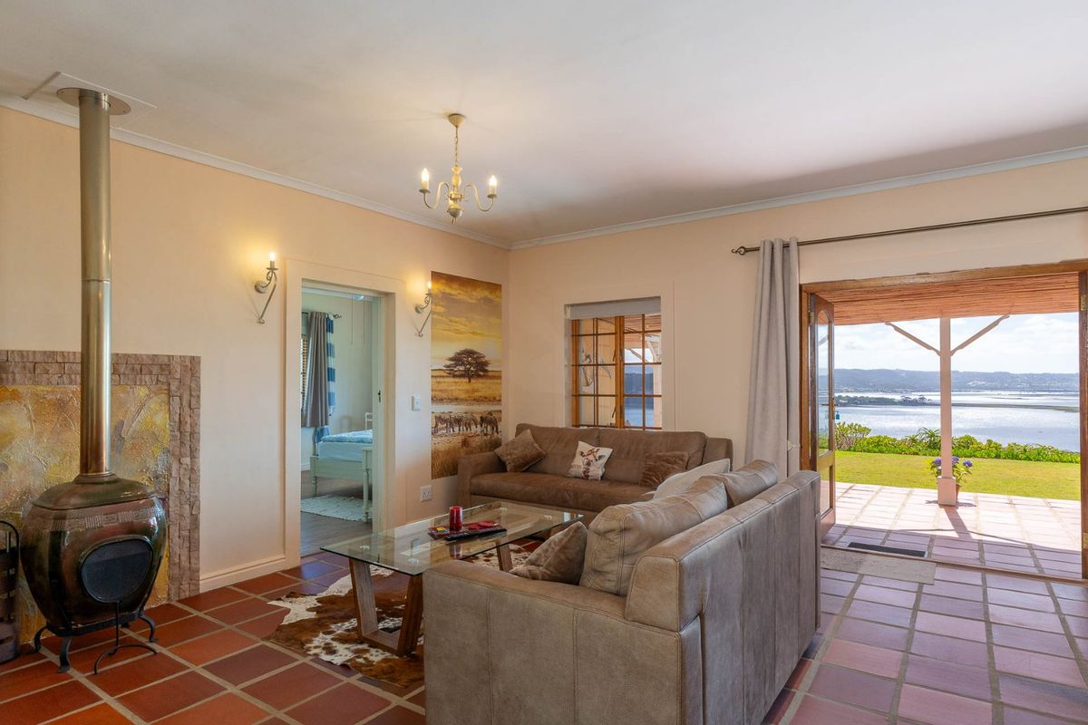 A cozy living room featuring a freestanding fireplace with stone surround, terracotta tile flooring, and direct access to a patio with scenic water views.