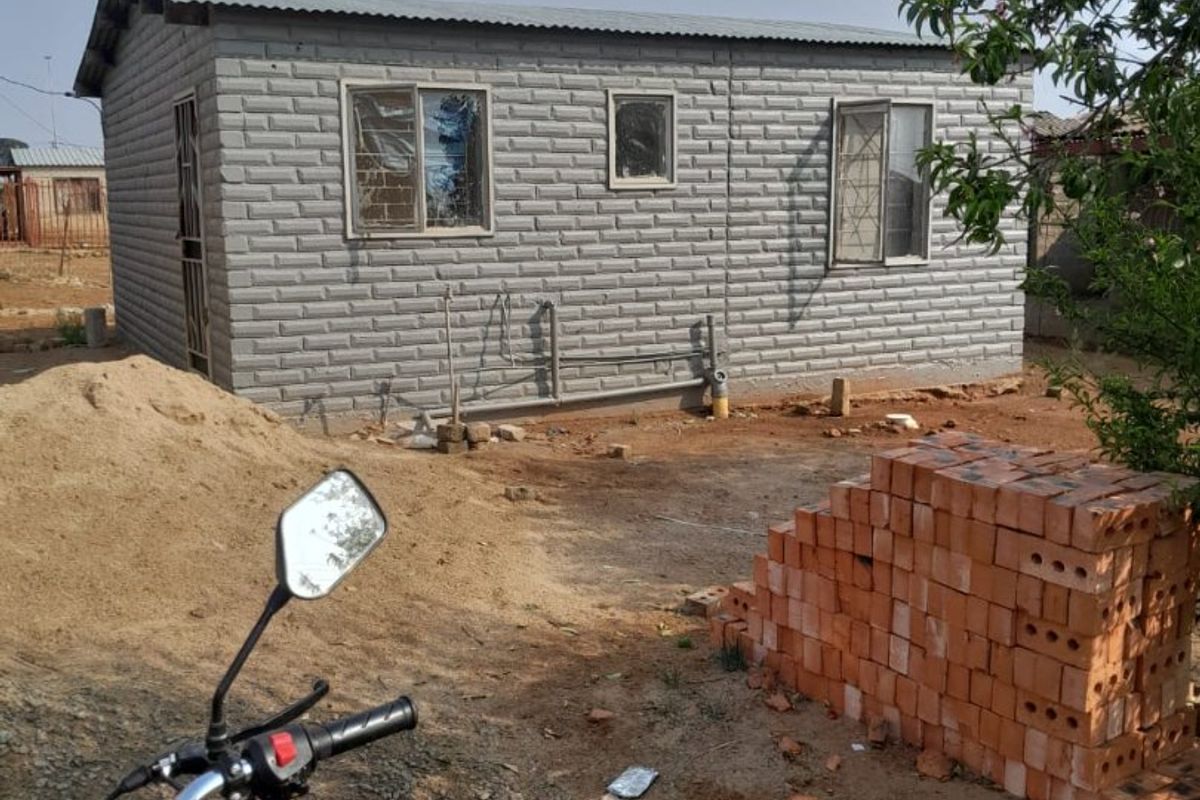 A view of the rear exterior of a small residential structure featuring exposed brick walls, corrugated metal roofing, and security-barred windows.