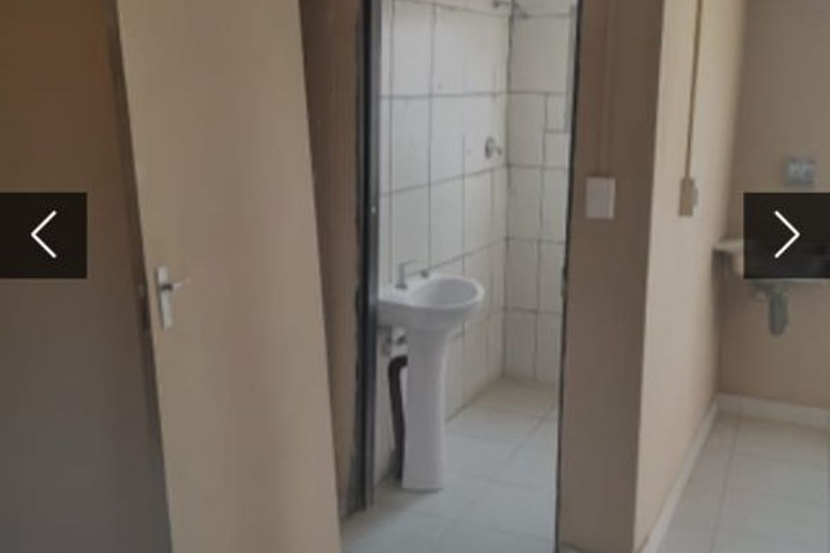 A basic bathroom featuring a pedestal basin and tiled shower enclosure, requiring cosmetic updates and repairs to finishes.