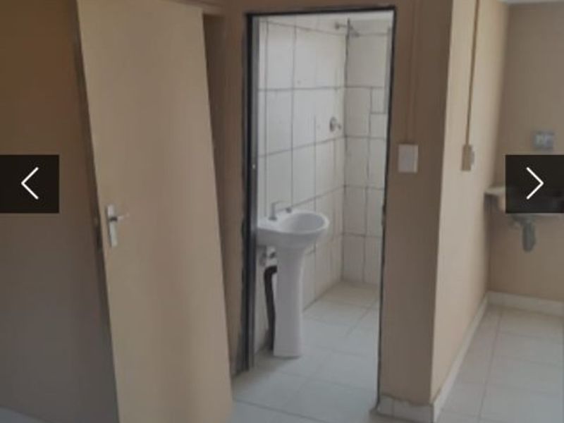 A basic bathroom featuring a pedestal basin and tiled shower enclosure, requiring cosmetic updates and repairs to finishes.
