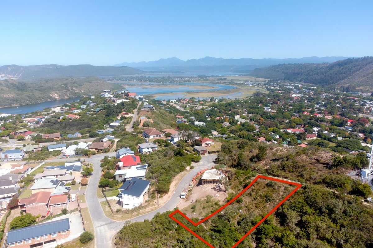An aerial view of a vacant residential plot situated on a hillside, offering expansive views of the surrounding landscape and coastal area.