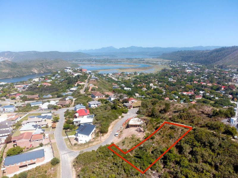 An aerial view of a vacant residential plot situated on a hillside, offering expansive views of the surrounding landscape and coastal area.