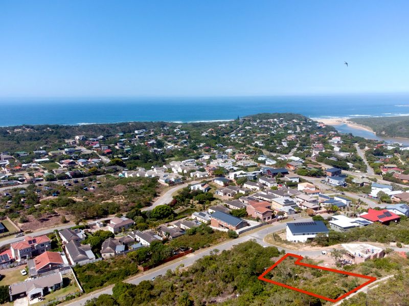 Aerial view of a vacant residential plot highlighted in red, situated within a coastal neighborhood with ocean views.