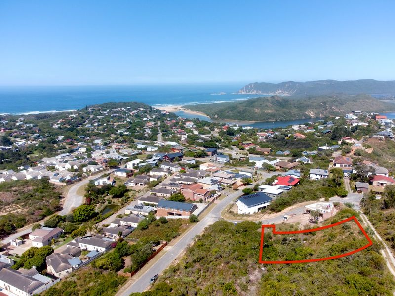 An aerial view of a vacant residential plot highlighted in red, situated in a coastal neighborhood with scenic ocean and landscape views.