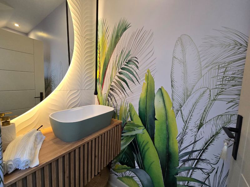 Modern bathroom featuring a stylish vessel sink, floating vanity, backlit circular mirror, and vibrant botanical feature wallpaper.